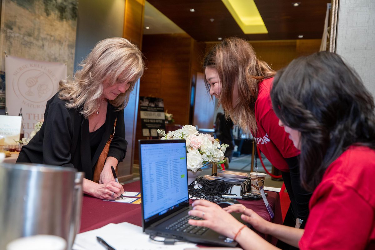 A guest signing a name tag at the EventPro Connect registration desk while team members check the guest list on a laptop